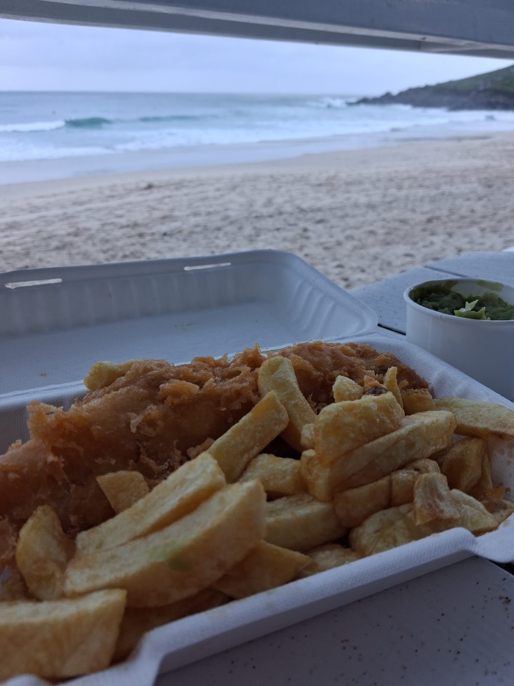 A takeaway box of chips beside the beach